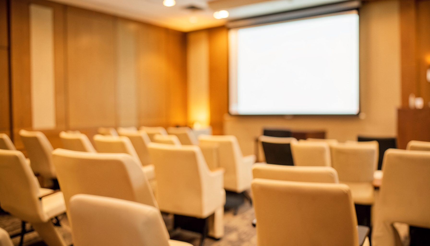 Soft-focus arrangement of conference-style chairs and a presentation screen in warm amber and cream tones